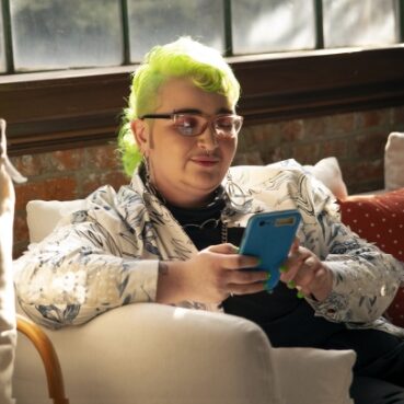 A genderqueer person looking at their phone green hair person with phone