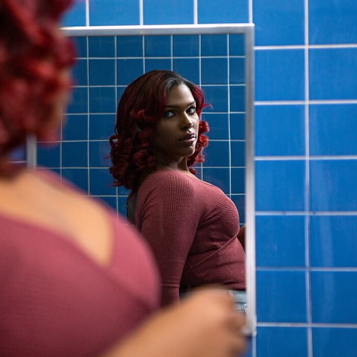 A person in a red shirt looking at mirror in a blue bathroom while looking at their own reflection
