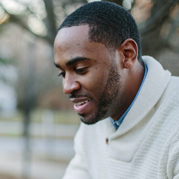 A black man with a white sweater sitting outside and smiling
