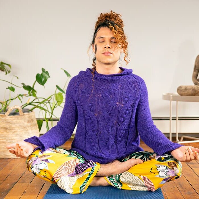 A person wearing a purple sweater and yellow pants sitting crosslegged on floor meditating