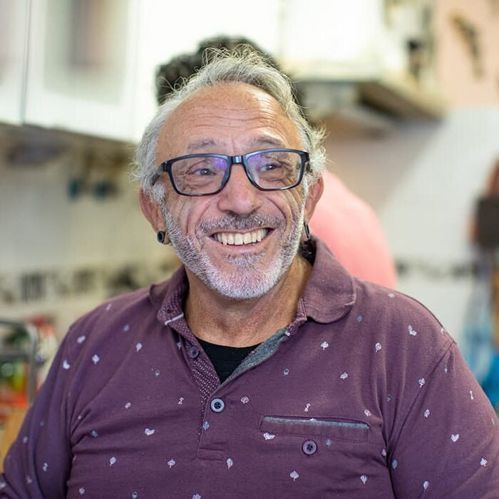 An older guy wearing a maroon shirt and glasses smiling at the camera