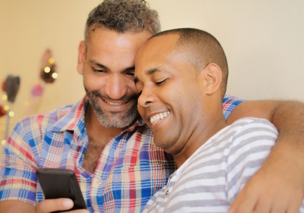 Two guys embracing and looking at a phone and laughing