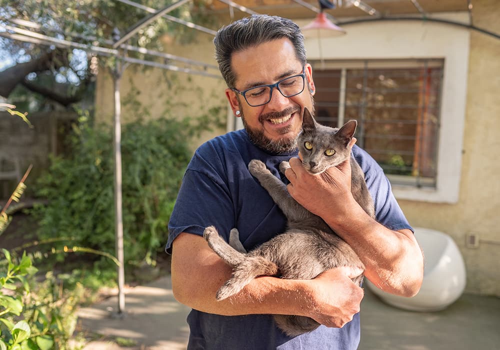 A guy with gray hair and an earing holding a cat and smiling