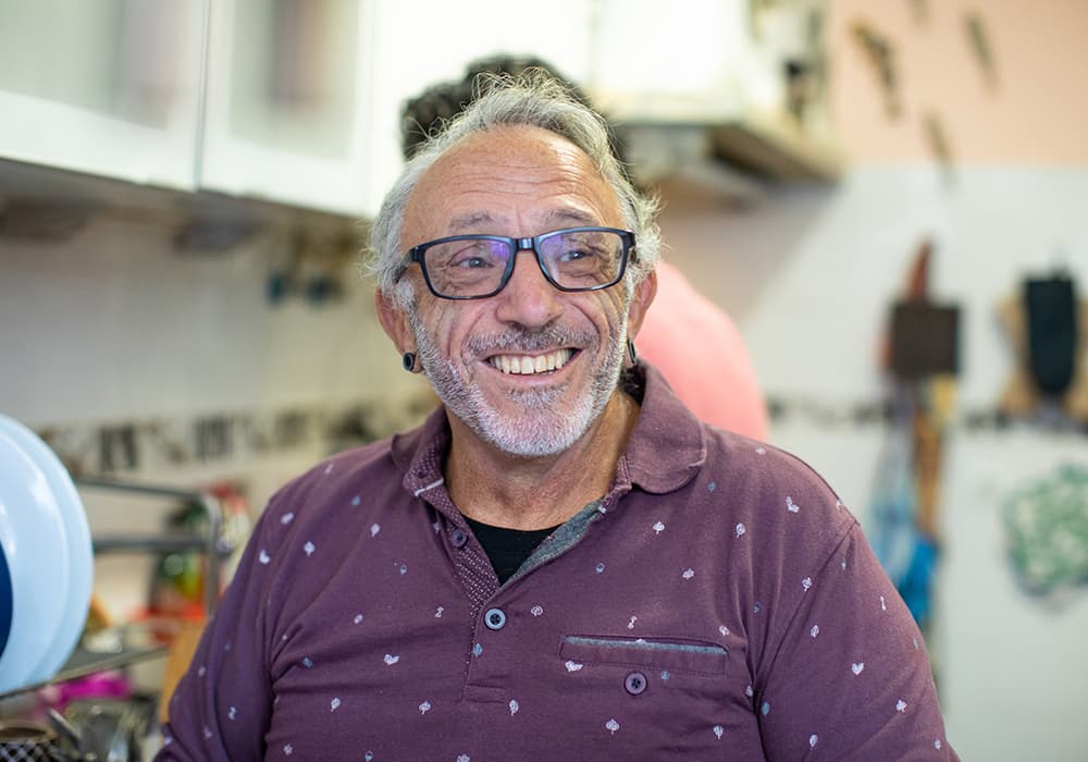 An older guy wearing a maroon shirt and glasses smiling at the camera