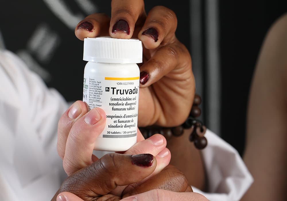 A small white bottle of truvada being held by someone wearing dark red nail polish